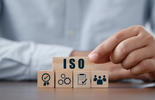 Eine Person platziert einen Holzblock mit der Aufschrift ‚ISO‘ auf weitere Blöcke, die verschiedene Aspekte eines Managementsystems symbolisieren